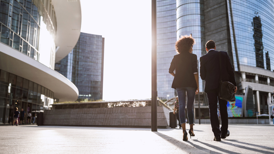 Professional man and woman walking together towards a city office building
