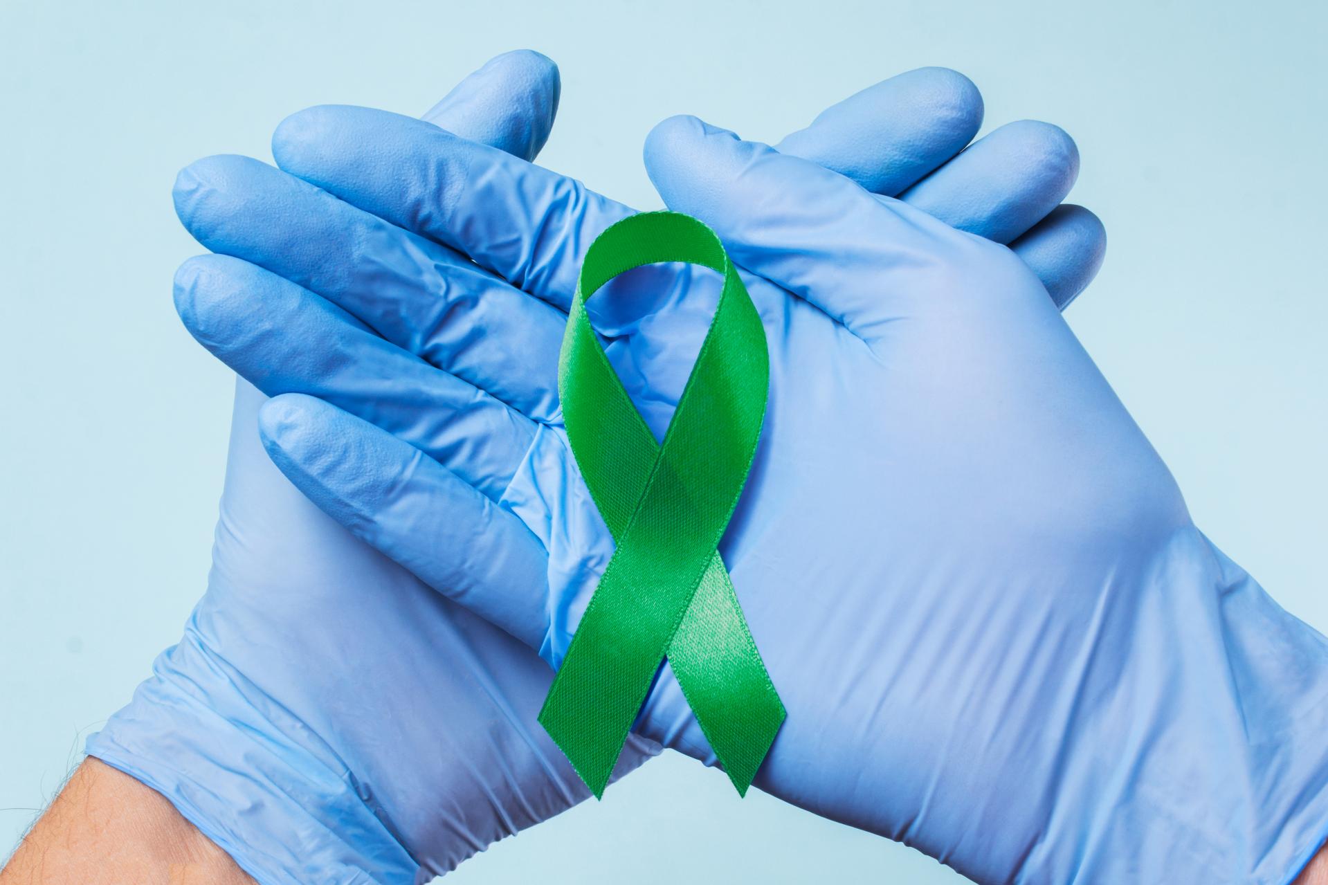 Blue gloves holding green mental health ribbon