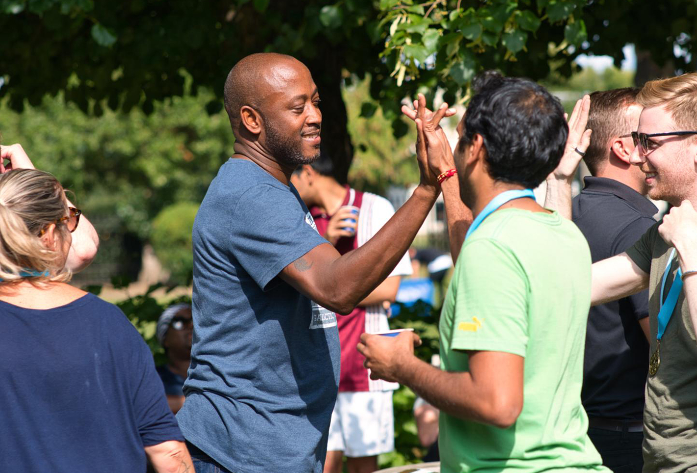 Employees high fiving as they enjoy a casual outdoor team social event