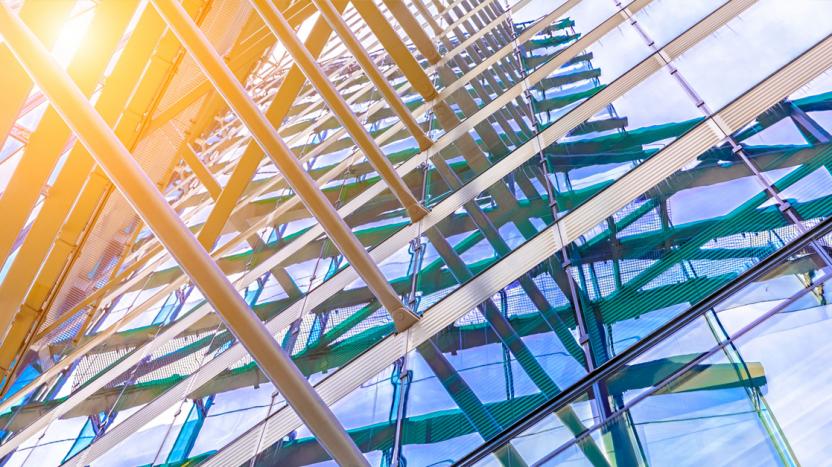 View from below a modern glass façade building, with sun shining from top left