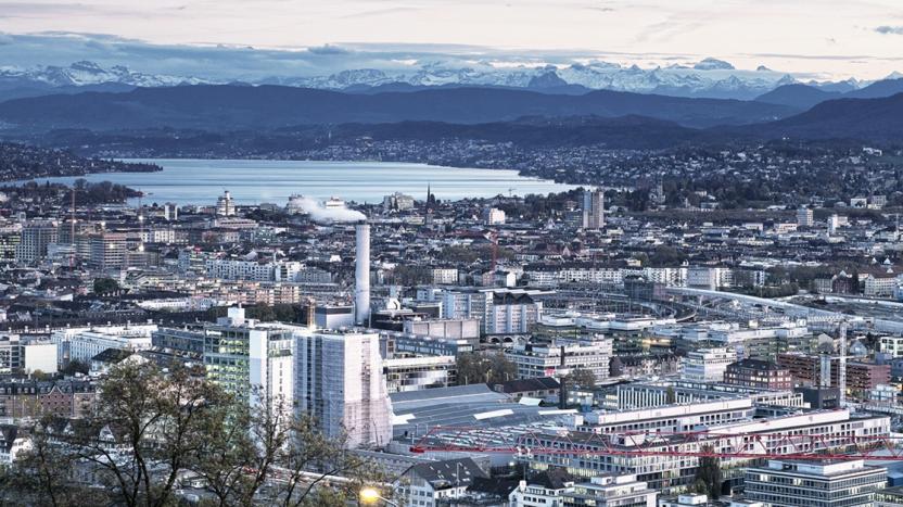 Blue toned cityscape with body of water and mountains in the background