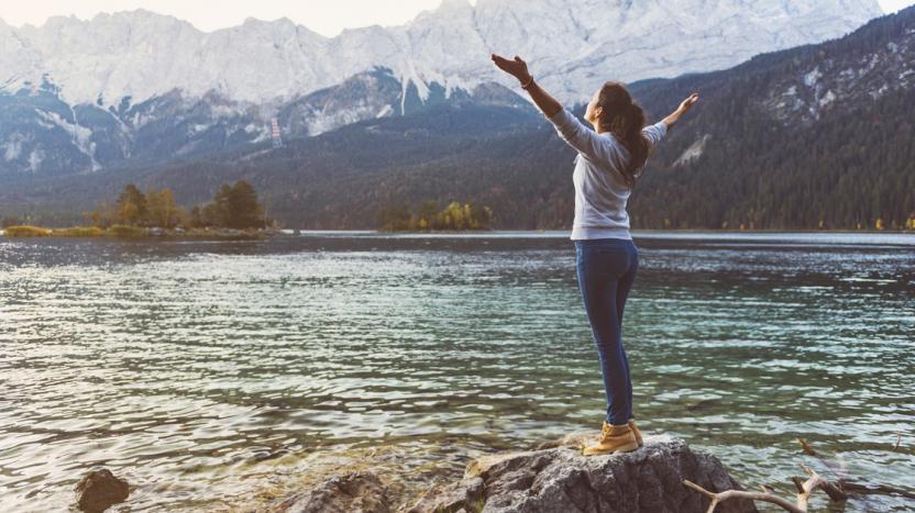 Woman standing on a rock overlooking the water with mountains in the background